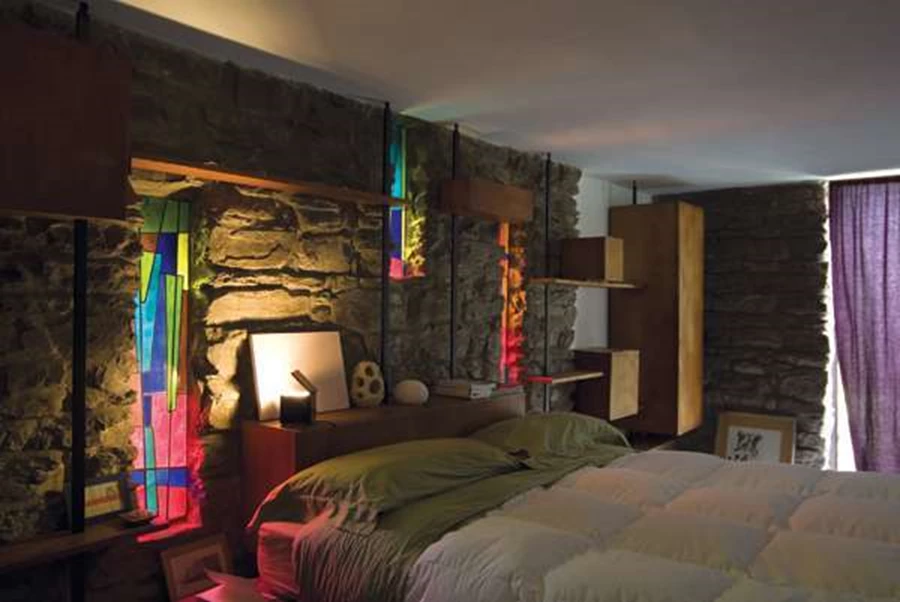 חדר השינה- הפתחים הצרים והארוכים עם הזיגוג הצבעוני קבועים בקיר האבן, ומערכת של מדפים וקופסאות 