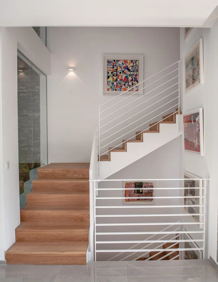 גרם המדרגות הממוקם לצד הפאטיו: מדרכי עץ אלון, מעקה ברזל לבן בעיצוב אוורירי-נקי, וציורים שמלווים את מהלכו עם תוכן אמנותי. 